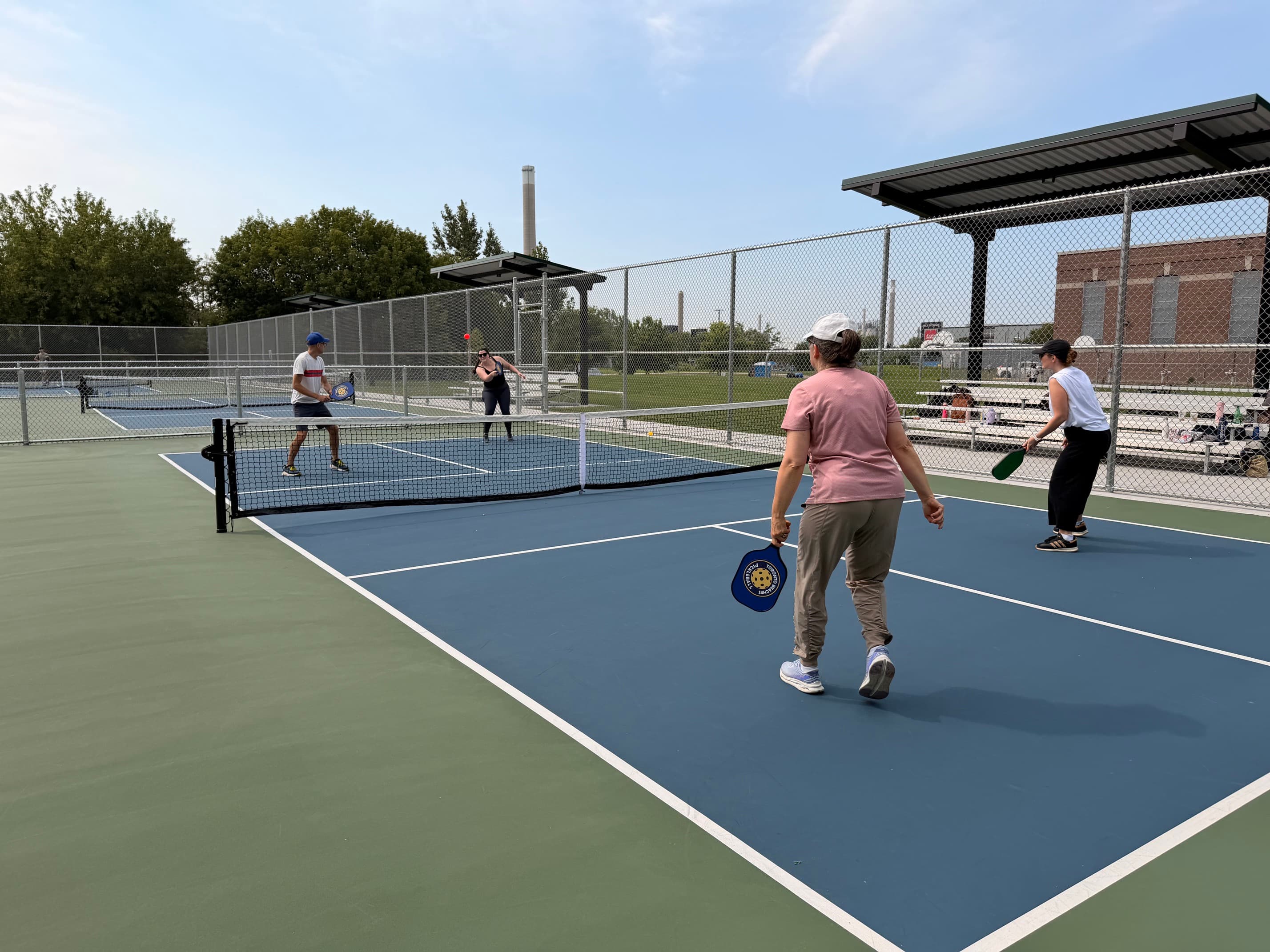 Four people playing a doubles pickleball match on a blue and green outdoor court.