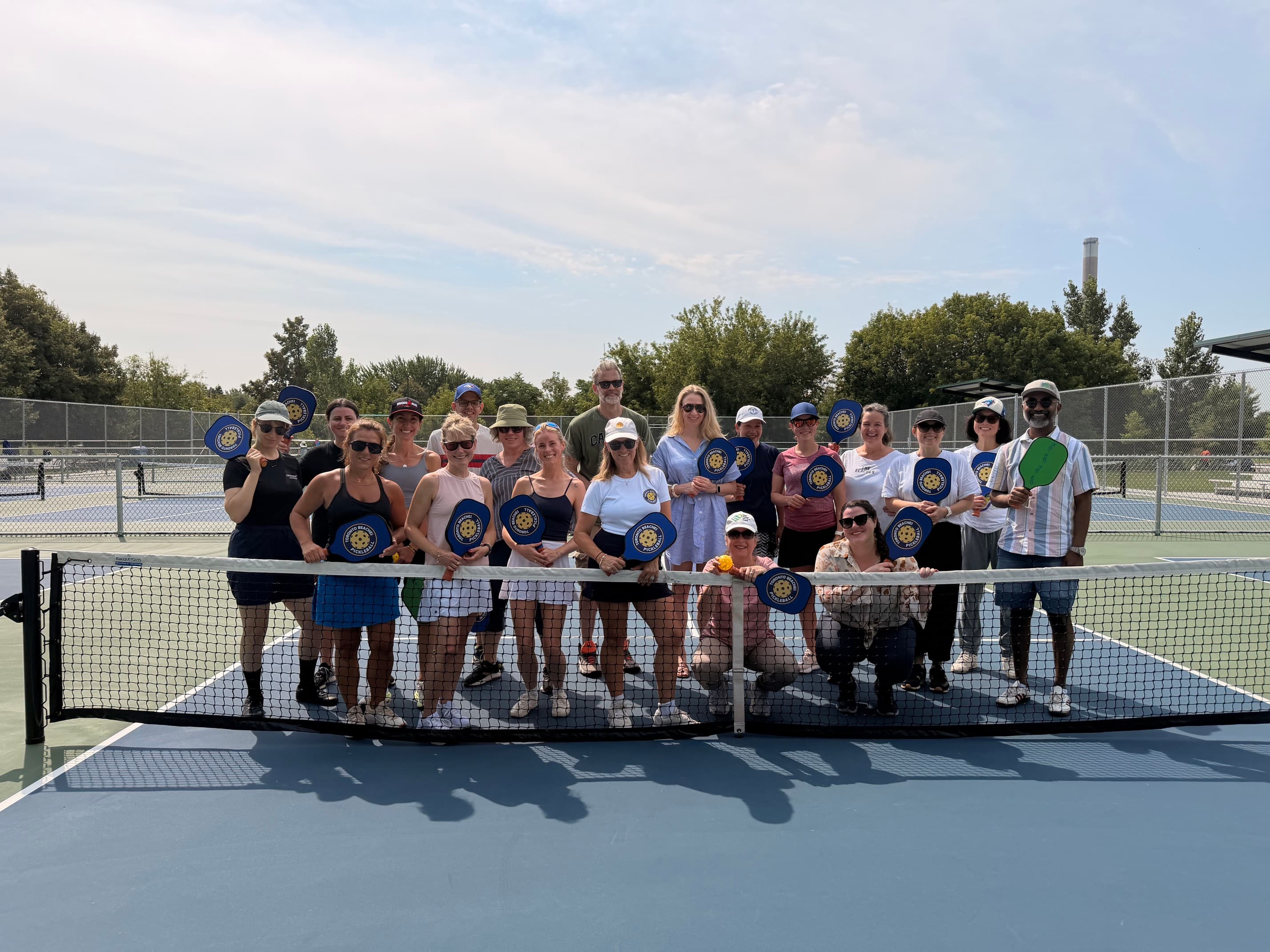 Large group of people posing with pickleball paddles on a blue court behind a net.