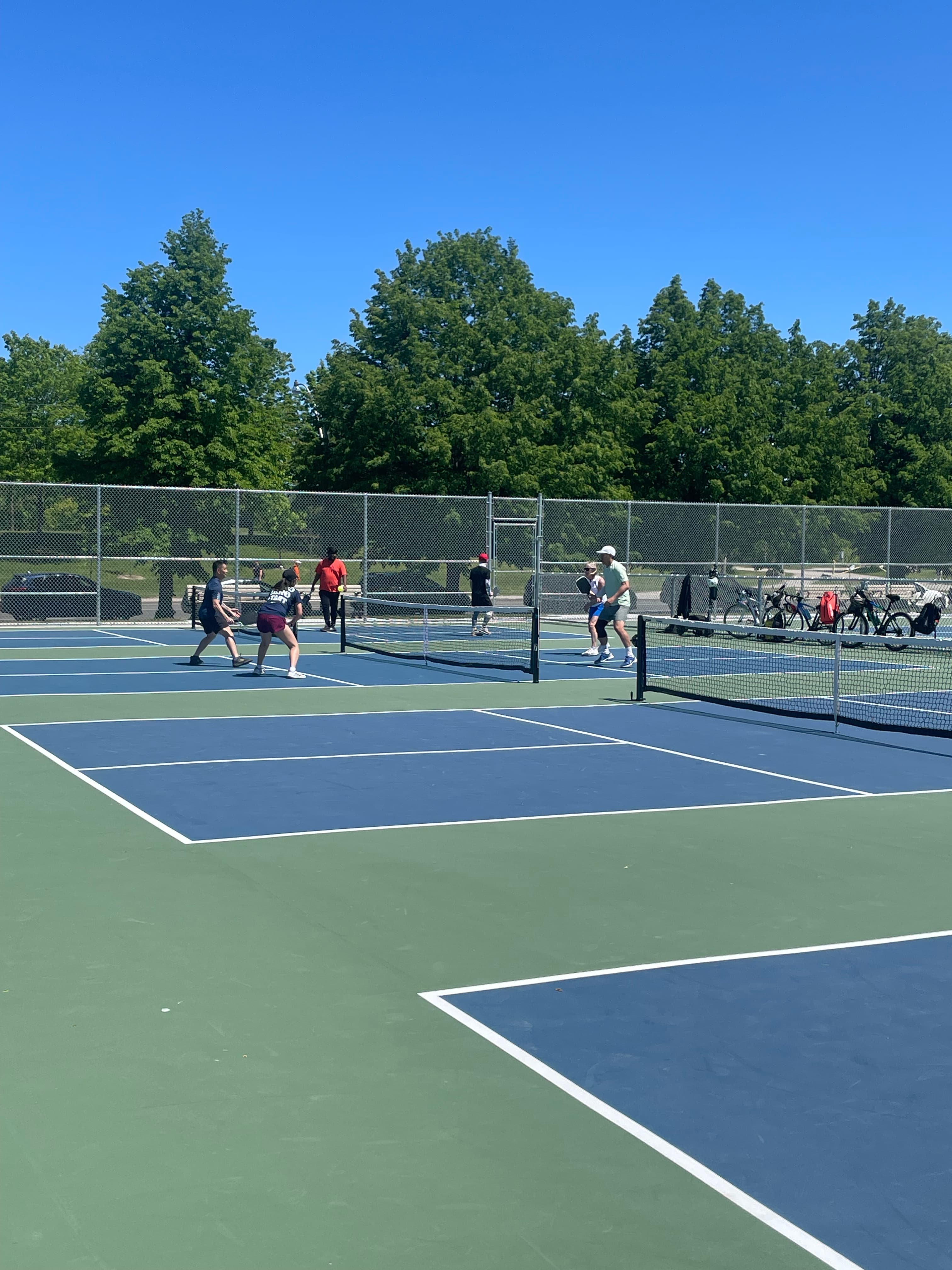 People playing pickleball on blue and green outdoor courts under a clear blue sky.